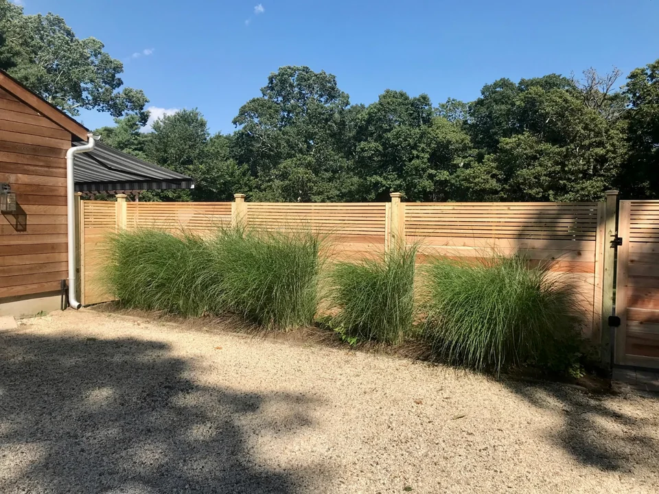Horizontal cedar fence beside ornamental grasses and a cedar-sided building in Westhampton, New York