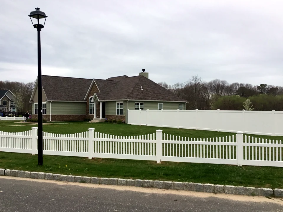 Side-yard view of a three-foot scalloped white PVC picket fence in Manorville, New York.