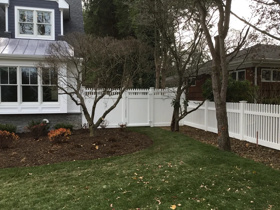 Wide landscaped view of mixed-height white PVC fencing in Locust Valley, New York