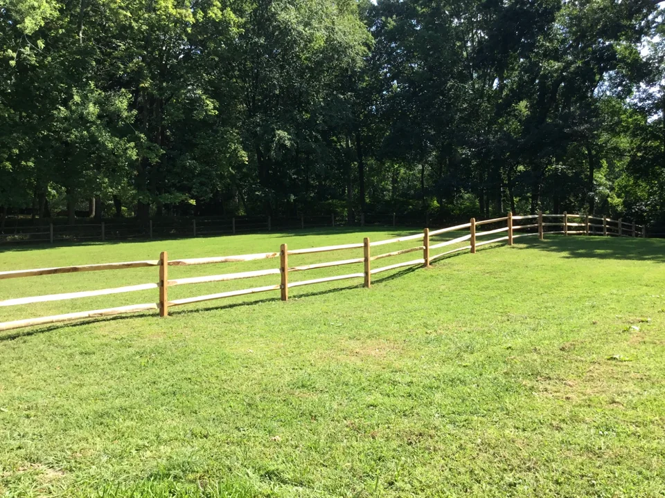 Three-rail split rail fence across a sloping Oyster Bay, New York property.