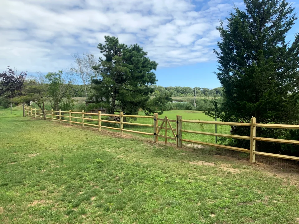 Three-rail split rail fence across an open Patchogue property.