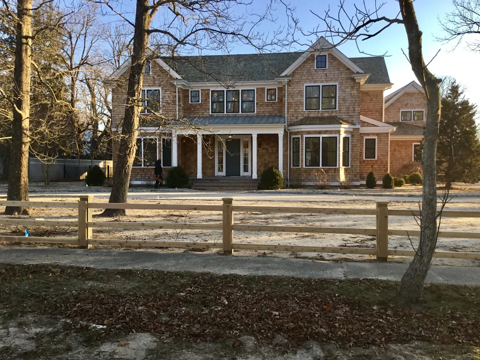 Wide house view of custom three-rail board fencing in Remsenburg, New York.