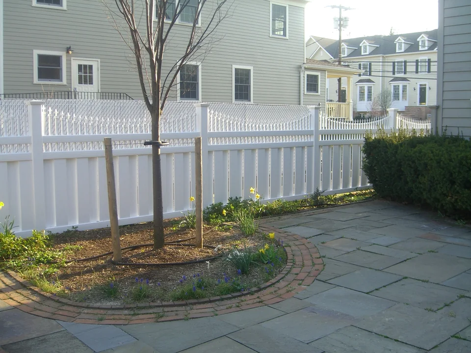 White shadowbox PVC fence with Victorian picket top bordering a landscaped garden in Oyster Bay, New York