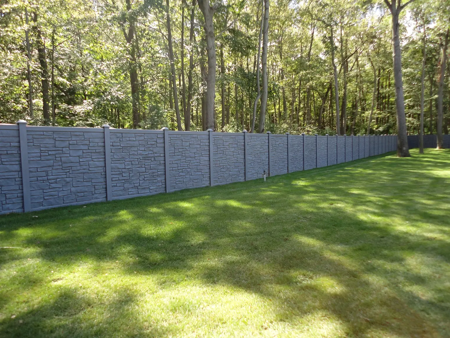 Long SimTek stone-look privacy fence across a wooded Suffolk County backyard