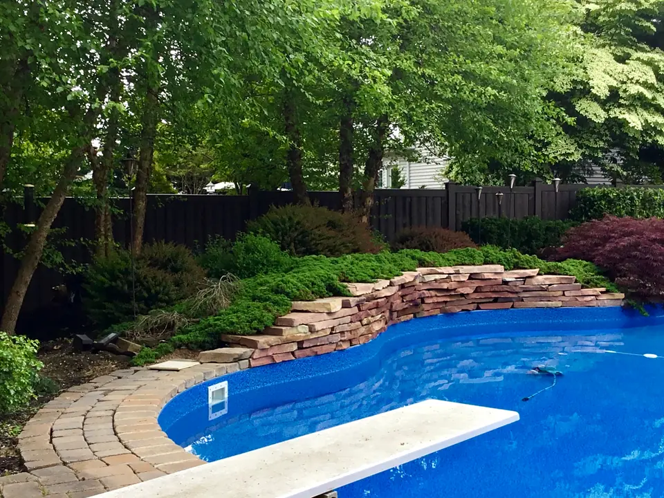 Dark wood-look molded privacy fence behind a landscaped swimming pool