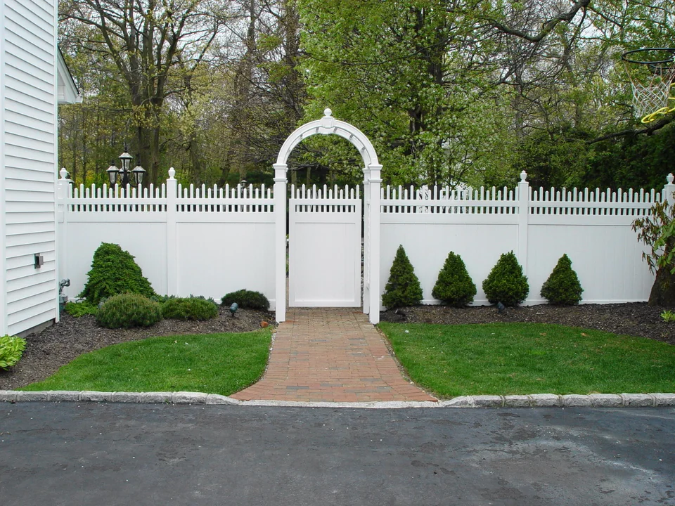 Six-foot white PVC privacy fence with alternating spindle top and arched arbor in Holbrook, New York