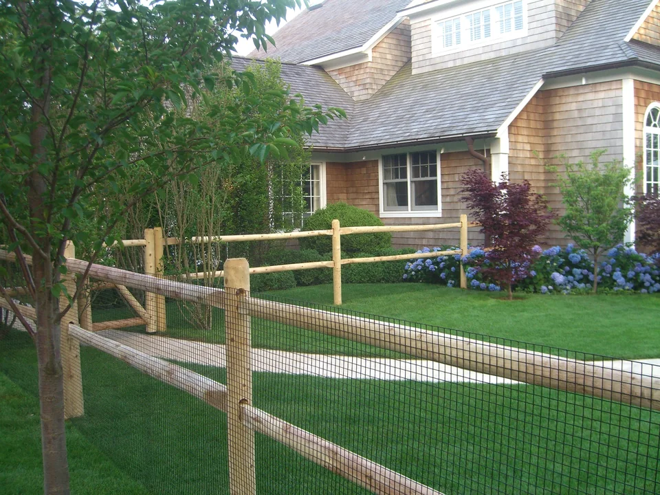 Two-rail round cedar post and rail fence with wire in Southampton, New York.