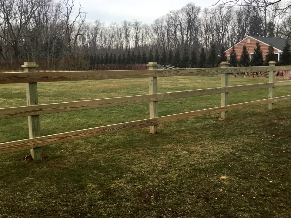 Pressure-treated three-rail board fence across an open Southold, New York property.
