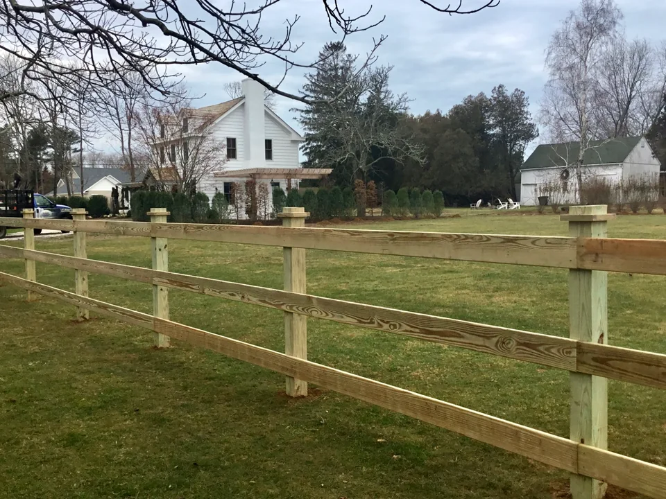 Pressure-treated three-rail board fence along a Southold property line.