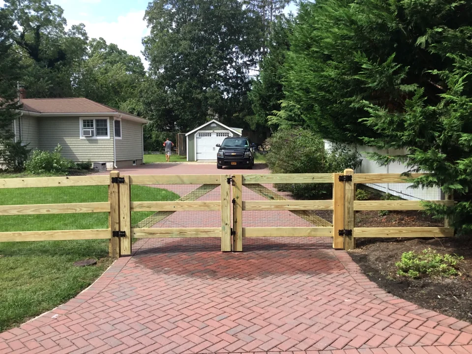 Driveway-side view of a three-rail board fence and gate in Speonk.