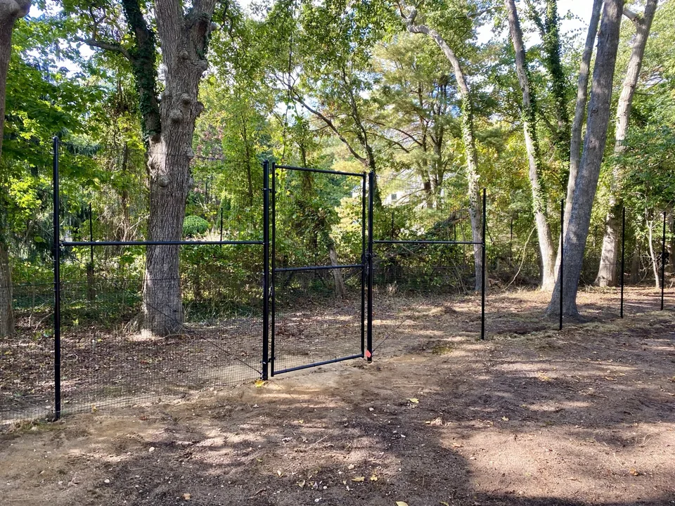 Black gate set into a stacked deer fence in a wooded setting