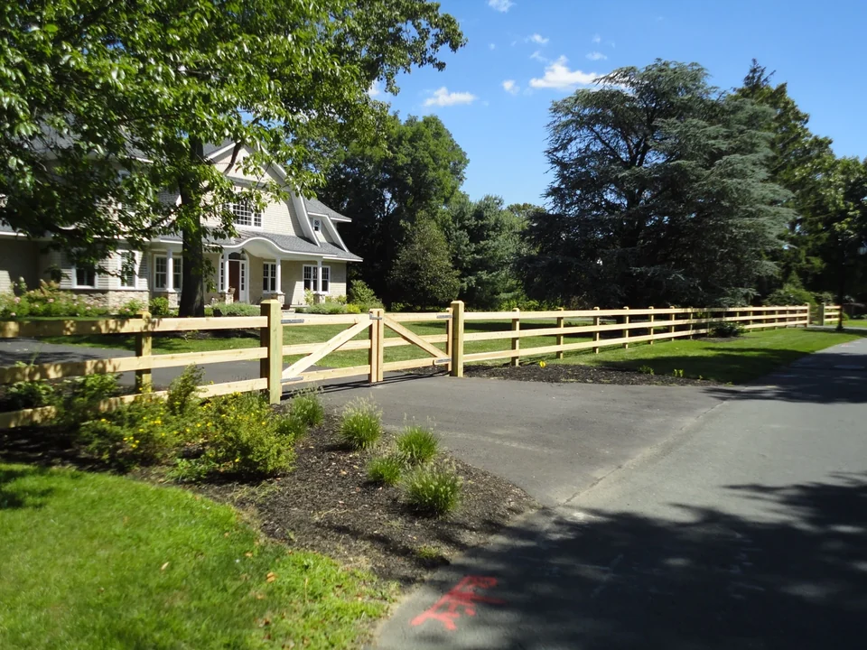 Three-rail cedar board fence following the landscaped property line in Bay Shore, NY