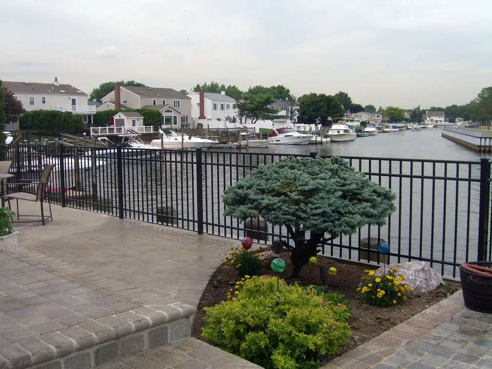 Black aluminum waterfront fence following a raised masonry patio beside a canal in Seaford, New York