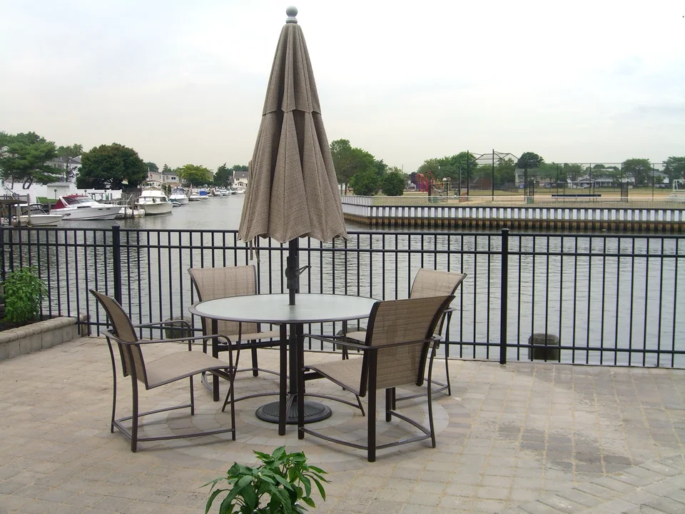 Black aluminum fence behind a patio dining area overlooking the water in Seaford, New York