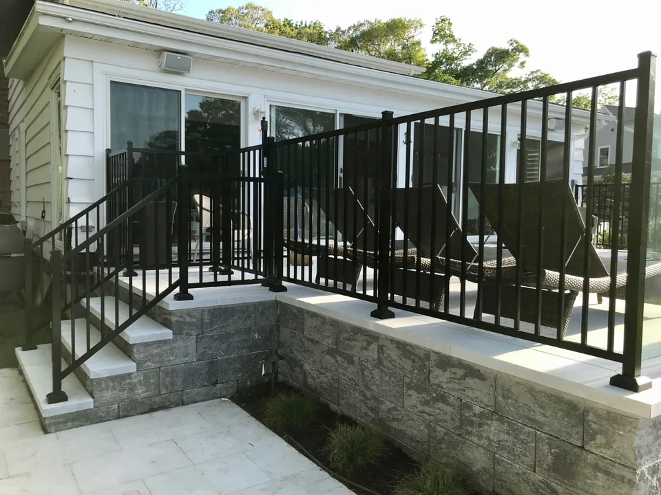 Black aluminum railing following the raised stone pool patio beside a Southold, New York home