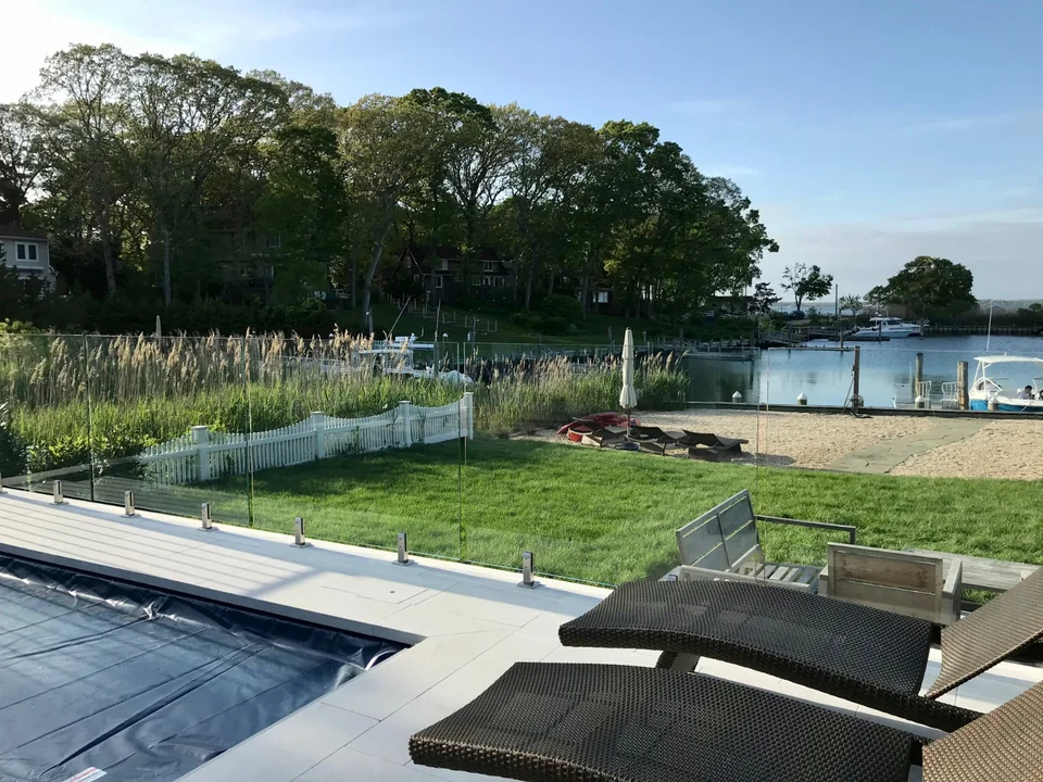 Frameless glass pool barrier with the lawn and waterfront beyond in Southold, New York.