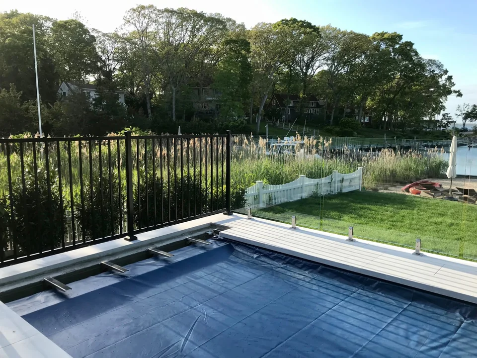 Pool and waterfront landscape viewed through frameless glass fencing in Southold, New York.