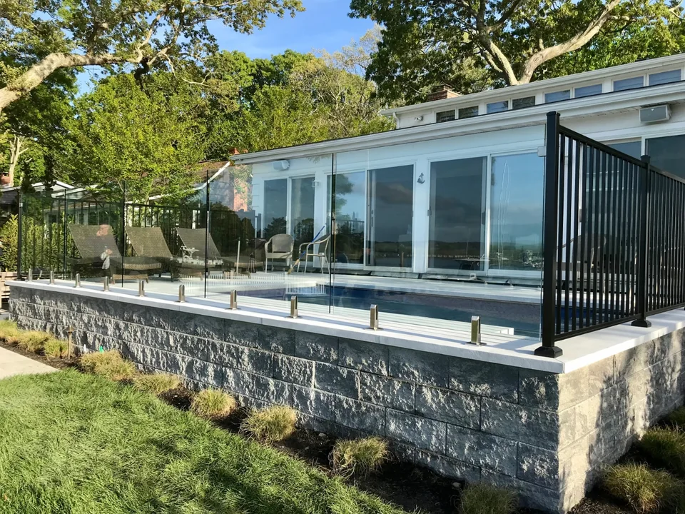 Wide exterior view of frameless glass panels around a raised waterfront pool patio in Southold, New York.