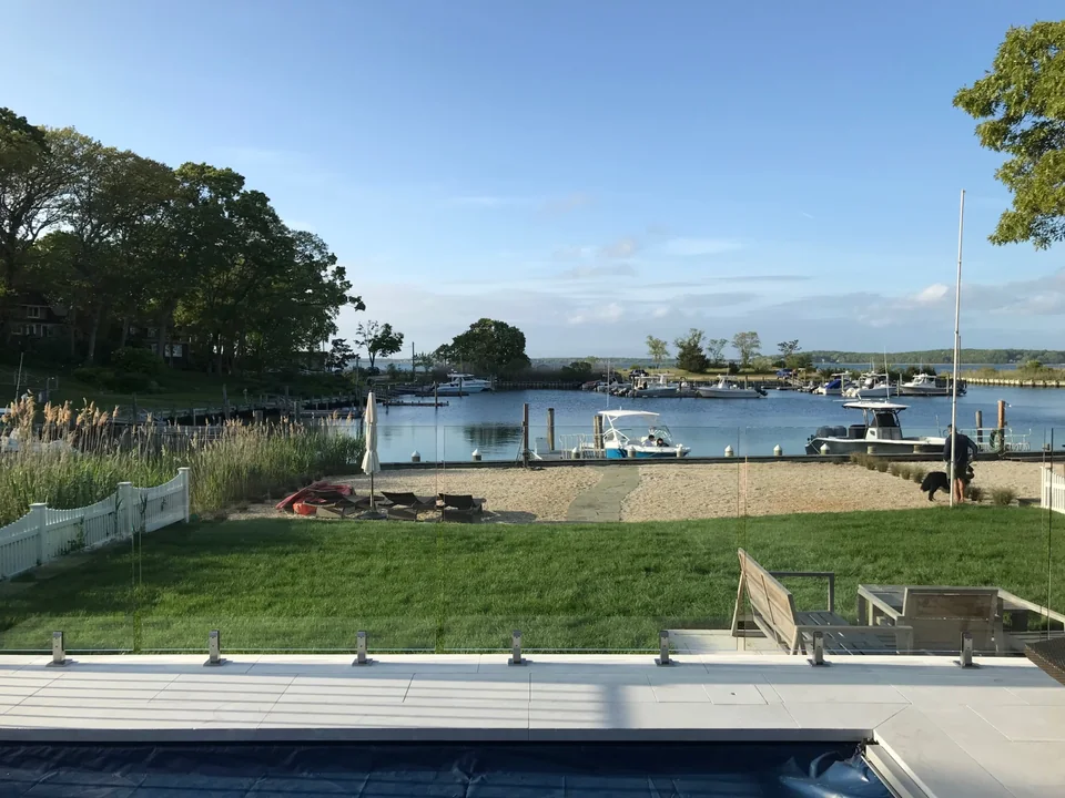 Waterfront view seen across the edge of a pool and frameless glass barrier in Southold, New York.