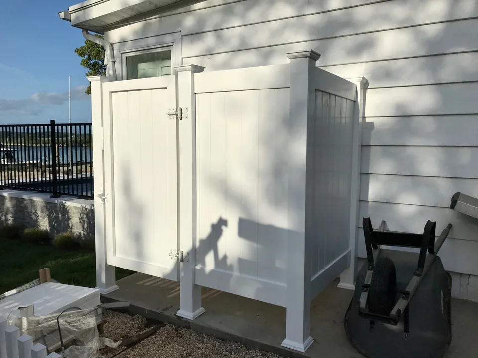 White PVC outdoor shower enclosure attached beside a waterfront home in Southold, New York.
