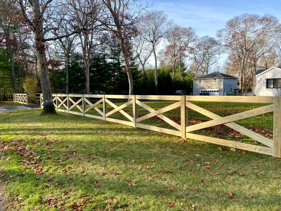 Custom pressure-treated crossbuck fence with wire infill across a Westhampton property.